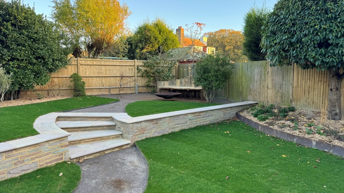 A garden landscape featuring a maintained lawn, with a seating area with a raised fire pit