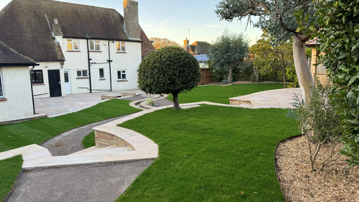 A back garden landscape featuring a turfed lawn, maintained trees and shrubs, and a patio