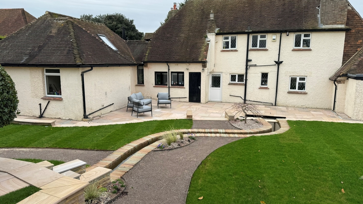 A garden landscape featuring a gravel path, patio and a unique water feature fed by a small stream